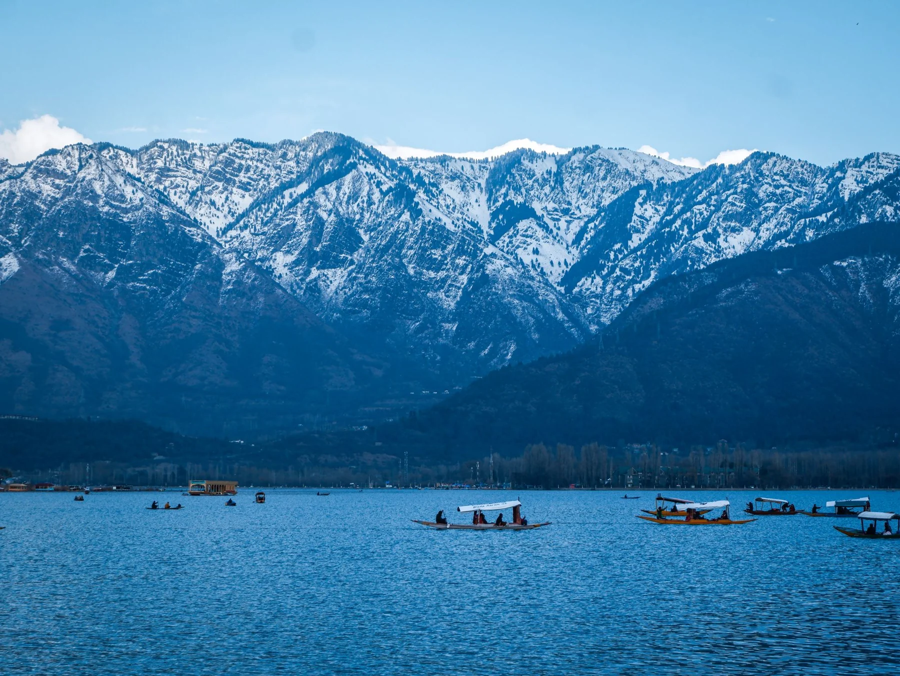 Blue waters and shikara boats on Dal Lake beneath the snow-covered mountains of Kashmir